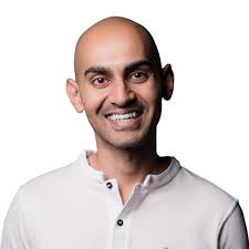 A bald man in a white shirt smiling while displaying his .COM domain.